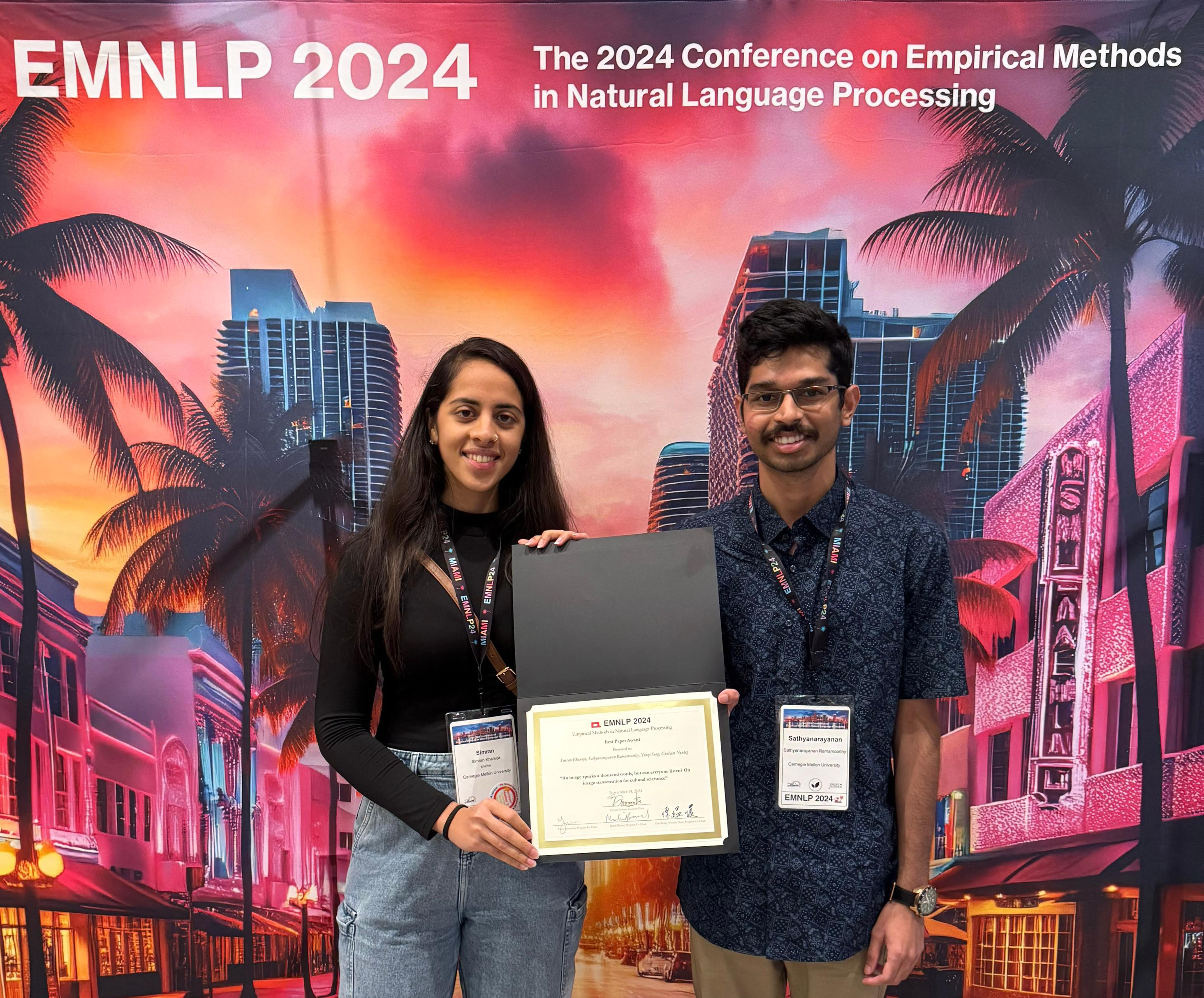 Simran Khanuja and her co-author pose with their Best Paper award certificate in front of an EMNLP-branded backdrop, purple and decorated with images evoking a Miami night