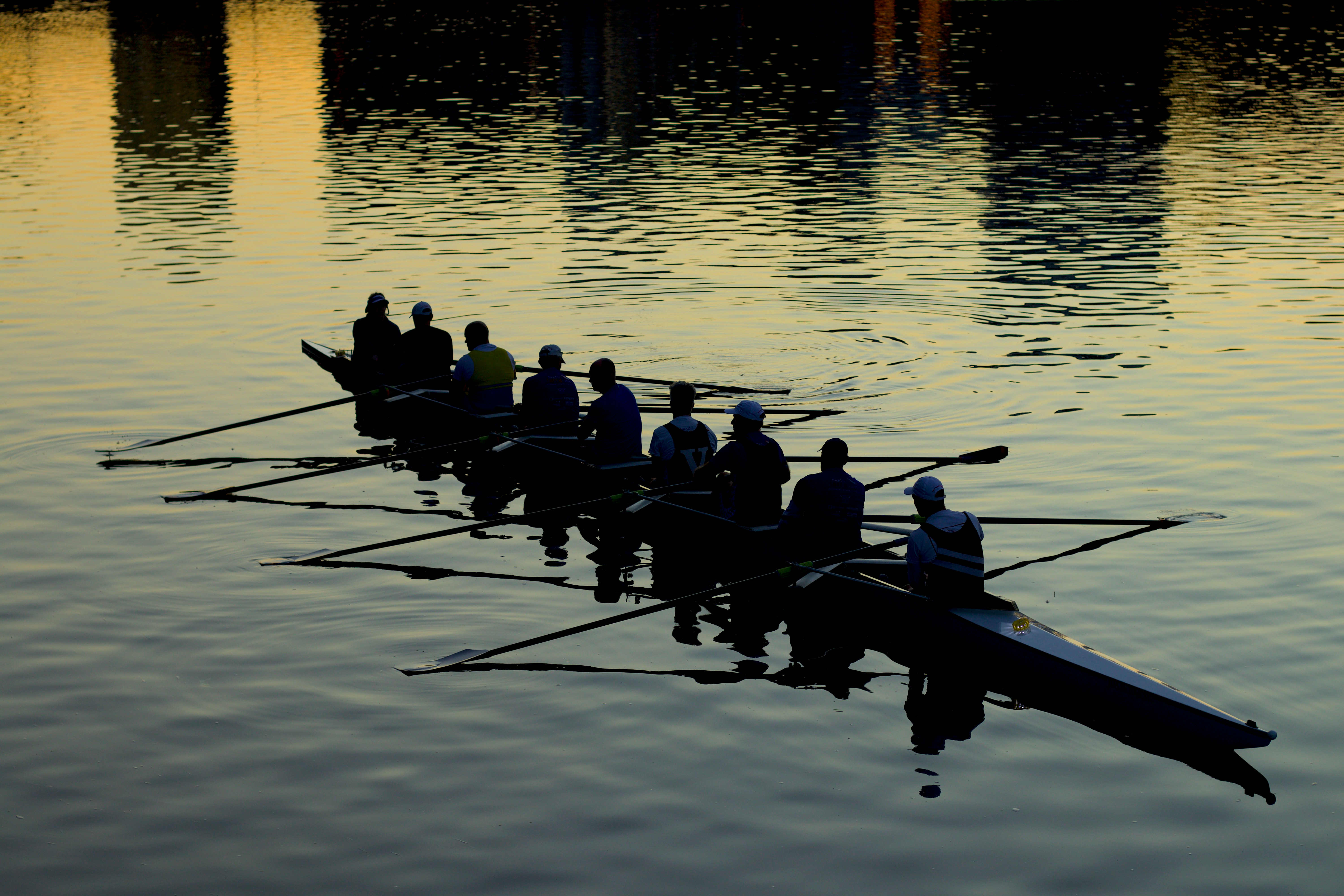 Photo of a crew team rowing their boar, silhouetted against an evening sky that reflects off the water